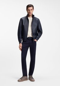 Δερμάτινο μπουφάν σε ναυτικό μπλε, με ψηλό γιακά και φερμουάρ. Συνδυασμένο με κρεμ πουκάμισο, ναυτικό μπλε παντελόνι και ανοιχτό καφέ αθλητικά παπούτσια με υφή.