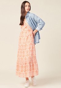 Maksimekkoinen oranssi ja valkoinen kuvio, jossa on kerroksellinen muotoilu. Yhdistetty vaaleansiniseen farkkutakkiin ja valkoisiin lenkkareihin.