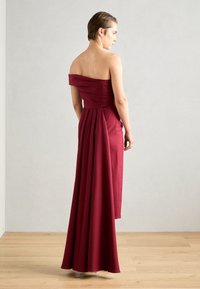 Rochie burgundy cu umeri goi, fustă plisată, cu un corset fără cusături și material fluid. Textură netedă, design până la podea, hardware minim.