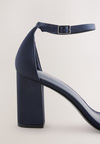 Tmavomodré sandále na vysokom opätku s remienkom okolo členka a prackou, s hrubým blokovým opätkom a hladkým povrchom.
