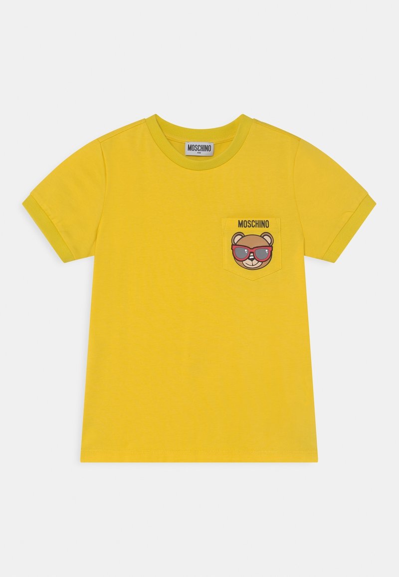 Camiseta de algodón amarilla con mangas cortas, que presenta un gráfico de un oso con gafas de sol en un bolsillo en el pecho. Logotipo de la marca impreso encima del bolsillo.