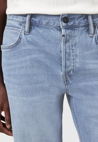 Jeans in denim azzurro chiaro con una vestibilità slim. Presentano cinque tasche, una chiusura con bottone e una leggera scoloritura sul tessuto.