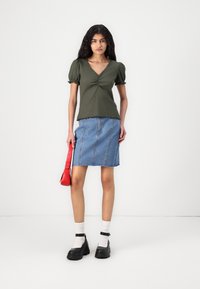 Roheline lühikeste varrukatega särk V-kaelusega ja kogumisdetailiga, kombineeritud hüppeliigmeni ulatuva helesinise teksaseelikuga. Mustad paksud kingad ja punane kott.