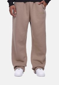Beige sweatpants with a relaxed fit, side pockets, and "DROPSIZE" embroidered in matching color. Worn with white sneakers.
