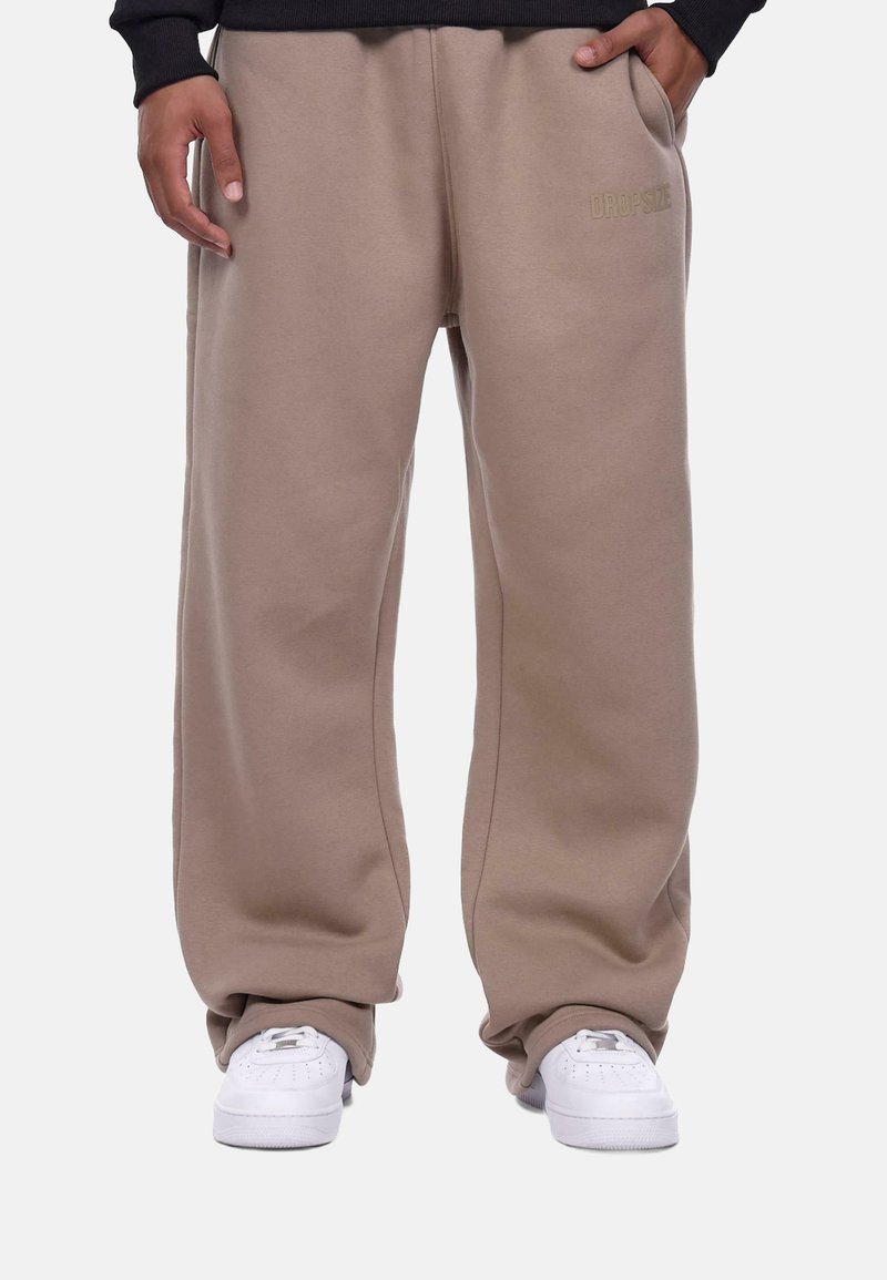 Beige sweatpants with a relaxed fit, side pockets, and "DROPSIZE" embroidered in matching color. Worn with white sneakers.