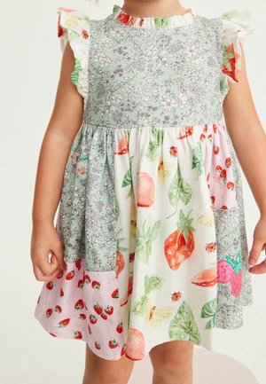 Kjole med lapværksmønstre med blomster- og frugtillustrationer, herunder jordbær, mariehøns og blade på et barns torso og arme.