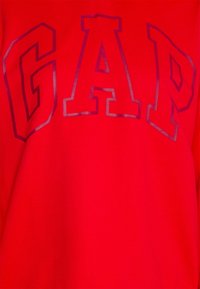 Tissu rouge avec de grandes lettres audacieuses bordées de noir formant le mot « GAP » au centre.