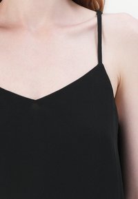 Gros plan d'une personne portant un haut noir à fines bretelles montrant les épaules et la clavicule.