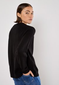 Maglione nero a maglia con vestibilità rilassata, maniche lunghe e polsini a coste. Indossato con jeans blu a vita alta, caratterizzati da una texture liscia.