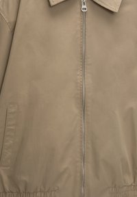 Beige bomber jacket featuring a zip front, collar, and elastic waistband. Smooth texture with side pockets and gathered cuffs.