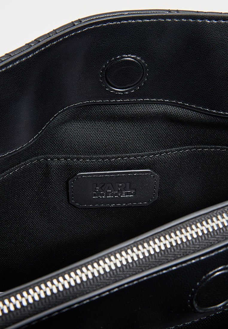 Intérieur d'un sac en cuir noir avec une doublure en textile, comportant un patch logo, une fermeture éclair et des détails de couture contrastés.
