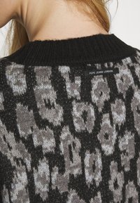 Svart stickad tröja med ett leopardsmönster i grått och beige. Etikett med "Pepe Jeans London" synlig på baksidan av halsringningen.