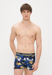 Vīriešu bokseršorti ar tumši zilu ziedu rakstu ar dzelteniem un baltiem akcentiem, ar platām elastīgām jostām, uz kuras ir uzraksts 'JACK & JONES'.