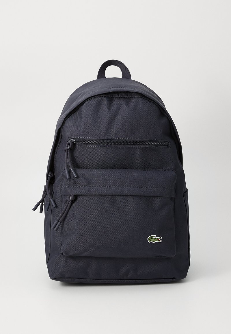 Marineblauwe stoffen rugzak met een afgeronde top, twee ritsvakken aan de voorkant en een logokleuraccent. Voorzien van verstelbare schouderbanden en een bovenste draaghendel.