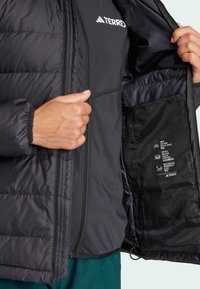 Black insulated jacket with zip closure, contrasting inner lining, and a label displaying care instructions. Features elastic cuffs.