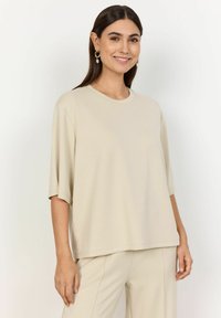 Beige oversized t-shirt with a rounded neckline and short sleeves. Made from soft fabric, featuring a relaxed fit and subtle side slits.