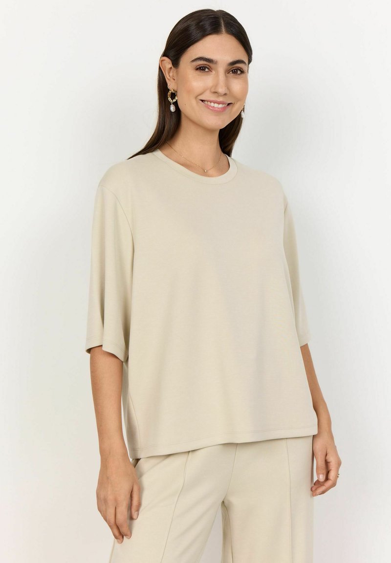Beige oversized t-shirt with a rounded neckline and short sleeves. Made from soft fabric, featuring a relaxed fit and subtle side slits.