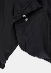 Schwarze Jacke mit glattem Stoff, Knopfverschluss mit metallischen Akzenten und elastischen Bündchen für einen sicheren Sitz.