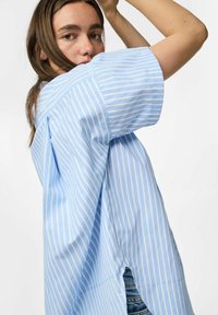 Jasnoniebieska i biała w paski, oversize'owa koszula, krótki rękaw, z bocznymi rozcięciami, o luźnym kroju i gładkiej bawełnianej fakturze.