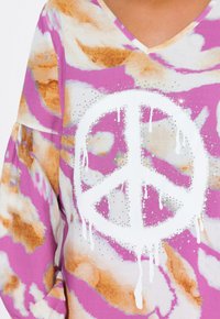 Top a scollo a V caratterizzato da un motivo astratto colorato con sfumature di rosa, bianco e marrone. Al centro, un simbolo della pace bianco adornato con dettagli argentati.