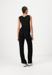 Débardeur noir ajusté avec de larges bretelles, associé à un pantalon noir ample et des chaussures de sport rose clair. Texture lisse, design décontracté.