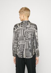 Long-sleeved shirt in black and white, featuring various geometric and abstract patterns. Soft fabric with a slightly loose fit and rounded hem.