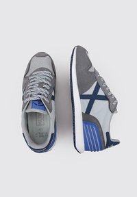 Zapatillas gris y azul claro que presentan materiales de malla y ante, con cordones y una suela texturizada, con acentos en marino y un logotipo en contraste.