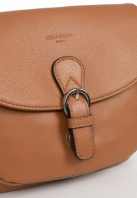 Borsa a tracolla in pelle color tan con finitura testurizzata, caratterizzata da una patta arrotondata, hardware in argento e un dettaglio della tracolla a forma di anello. Logo del marchio in rilievo.