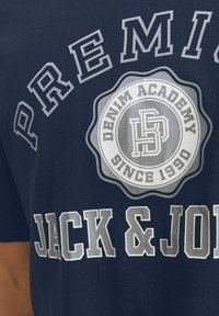 Tamnoplava pamučna majica s velikim bijelim i sivo tekstom: "PREMIUM JACK & JONES" i okruglim logotipom s natpisom "DENIM ACADEMY SINCE 1990."