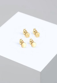 Zlate uhane na zatič, ki predstavljata dva različna dizajna: en je okrogel in gladek, drugi pa teksturiran z vzorcem faset.