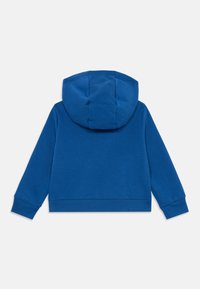 Fato azul feito de tecido suave, apresentando um grande capuz, punhos canelados e uma barra canelada. Nenhos detalhes frontais visíveis.