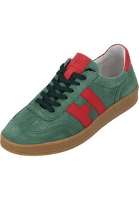 Gröna mockaskor med röda accenter och snörning, som har en gummisul och ett sydd mönster. Logotyp präglad på tungan.