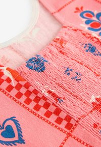 Roosa kangas sisaldab tekstureeritud ala, kus on punased ja sinised lillemustrid ning ruudulised aktsendid. Kaelus on ümmargune ja pehme servaga.
