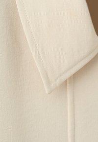 Gros plan d'un tissu beige plié avec une texture de tissage diagonal visible et une couture le long du bord.