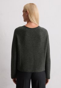 Dunkelgrauer, strukturierter Pullover mit weitem Ausschnitt und langen Ärmeln, kombiniert mit gestreiften Hosen. Der Saum ist hinten leicht verkürzt.