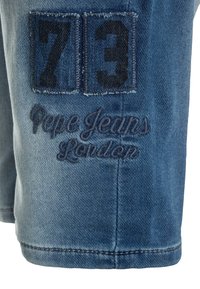 Shorts de denim de color azul con parches cosidos que muestran "73" y "Pepe Jeans London" en hilo oscuro.