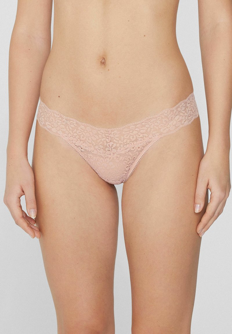String en dentelle rose pâle, arborant un motif floral et une large ceinture en dentelle. Léger et transparent avec une coupe arrondie.