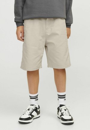 Beige katoenen shorts met een losse pasvorm, voorzakken en een rechte snit. Draagt mooie zwarte en witte sport schoenen en gestreepte sokken.