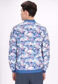 Giacca bomber floreale bianca, con stampe tropicali blu e rosa, colletto e polsini a coste blu, dal taglio morbido.