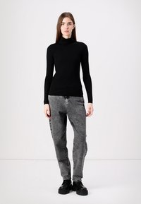 Μαύρο ριγμένο μακρυμάνικο πουλόβερ με λαιμόκοψη τύπου τζόκερ, συνδυασμένο με ξεθωριασμένο γκρίζο τζιν ψηλής μέσης και ογκώδεις μαύρες μπότες, πάνω σε λευκό φόντο.