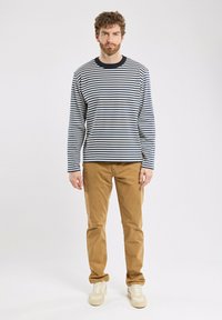Gestreiftes Langarmshirt in Marineblau und Weiß, kombiniert mit Khakihosen. Verfügt über einen Rundhalsausschnitt und eine lässige Passform. Sneakers in Creme mit beigen Akzenten.