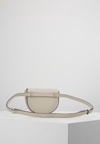 Pyöreä olkalaukku vaaleanbeigeä teksturoidusta nahasta, jossa on tasainen, taitettava läppä ja säädettävä hihna; minimalistisia designeyksityiskohtia.