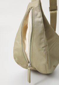Borsa a tracolla in nylon khaki con una superficie liscia, dotata di una zip e un tirante prominenti, e una forma a goccia elegante.