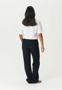 White short-sleeve shirt and black tailored pants viewed from the back, highlighting the relaxed fit and smooth texture of both garments.
