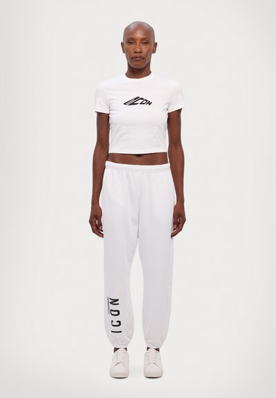 T-shirt blanc court avec un motif "ICON" noir, associé à un pantalon de survêtement blanc ample avec l'imprimé "ICON" sur le côté et des baskets blanches.