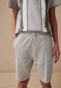 Vaaleanharmaa puuvillasekoiteasu, johon kuuluu lyhythihainen yläosa pystysuorilla raidoilla ja siihen sopivat, sivutaskuilla varustetut elastisella vyötäröllä varustetut shortsit.