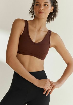 Brun sportbh med V-ringning, texturerad paneldesign och breda axelband, kombinerad med högmidjade svarta leggings. Slätt tyg genom hela plagget.