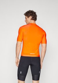 Cyklistický dres s krátkym rukávom v jasne oranžovej farbe, vyrobený z hladkého, elastického materiálu. Obsahuje zadnú kapsu a kontrastné čierne šortky s vertikálnymi pruhmi.
