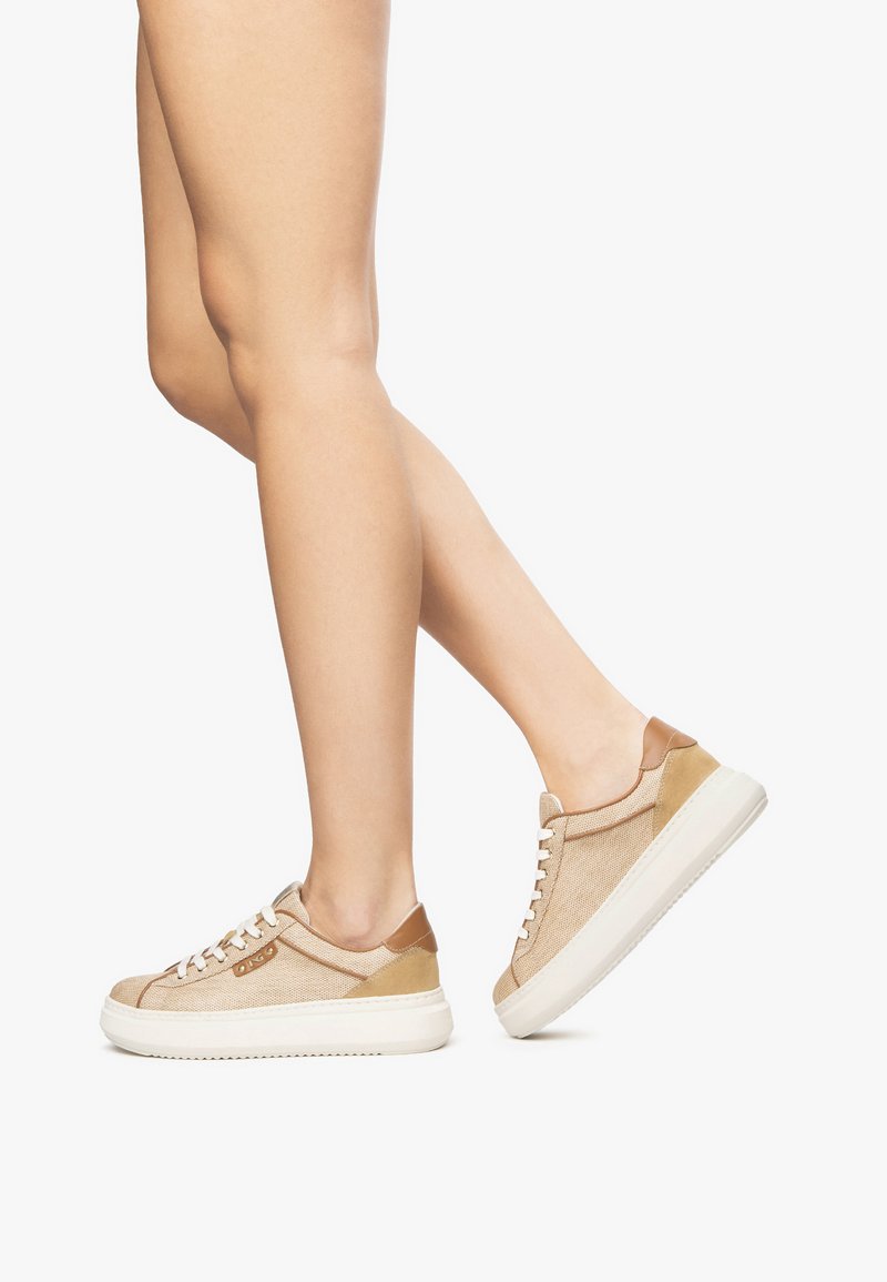 Baskets en toile beige avec accents en cuir, semelles en caoutchouc blanches, bouts ronds et lacets plats, présentant une surface texturée.