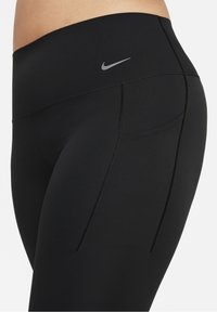 Czarne legginsy wykonane z elastycznego materiału, z wysokim stanem, płaskimi szwami i małym szarym logo Nike z tyłu.